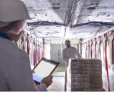 Person checking information on electronic tablet while college moves pallet of sacks in the background.