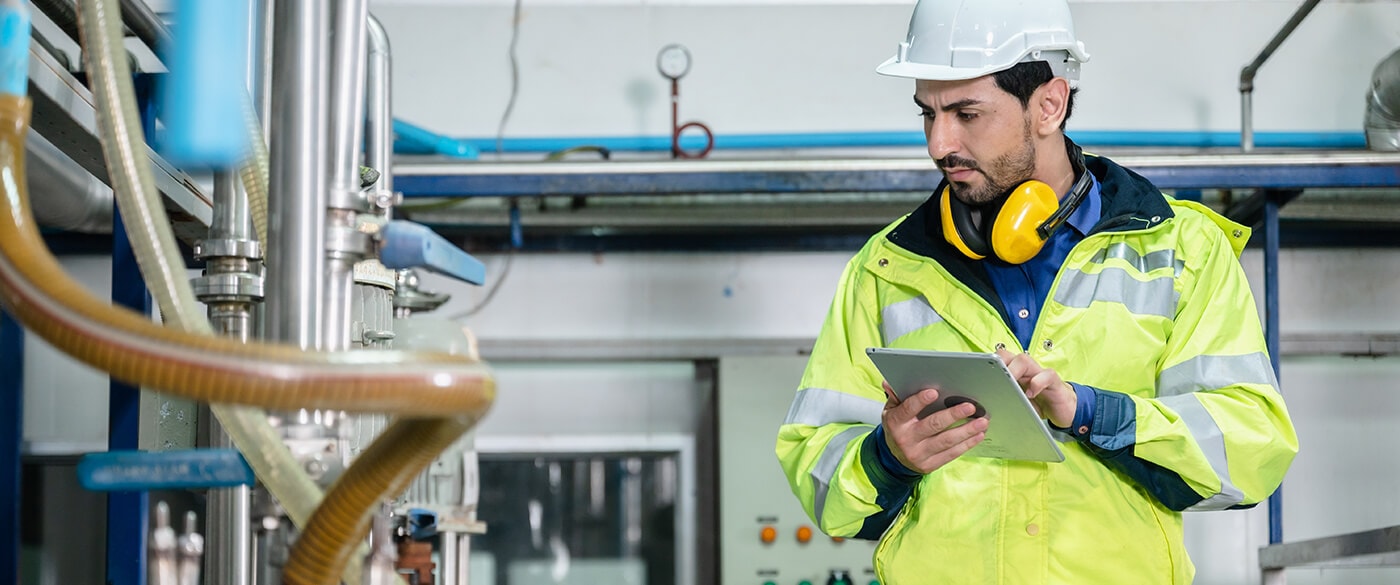 A man wearing PPE and holding a tablet, inspects pipes inside a building