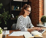 A woman wearing glasses types on a laptop