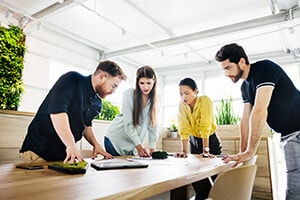 A group of office workers standing around a table, looking down at documents