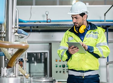 A man wearing PPE and holding a tablet, inspects pipes inside a building