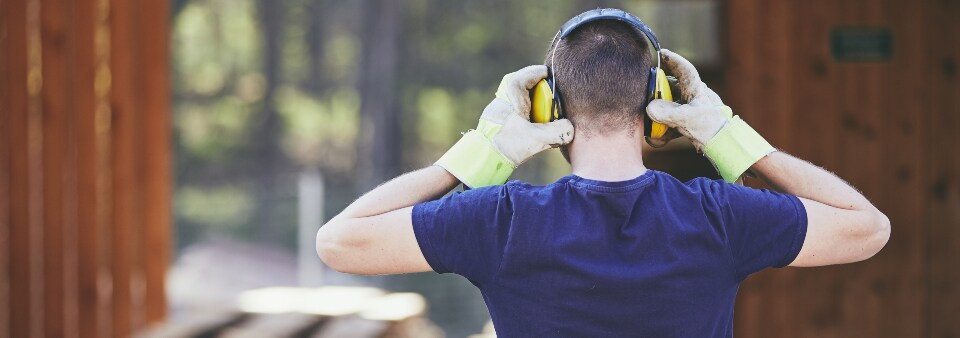 Man holding ear defenders with protective gloves.