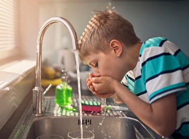 child drinking water from a tap, highlighting it's safe and passes regulations