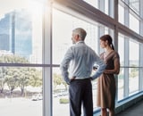 Two people in an office standing and looking out a window