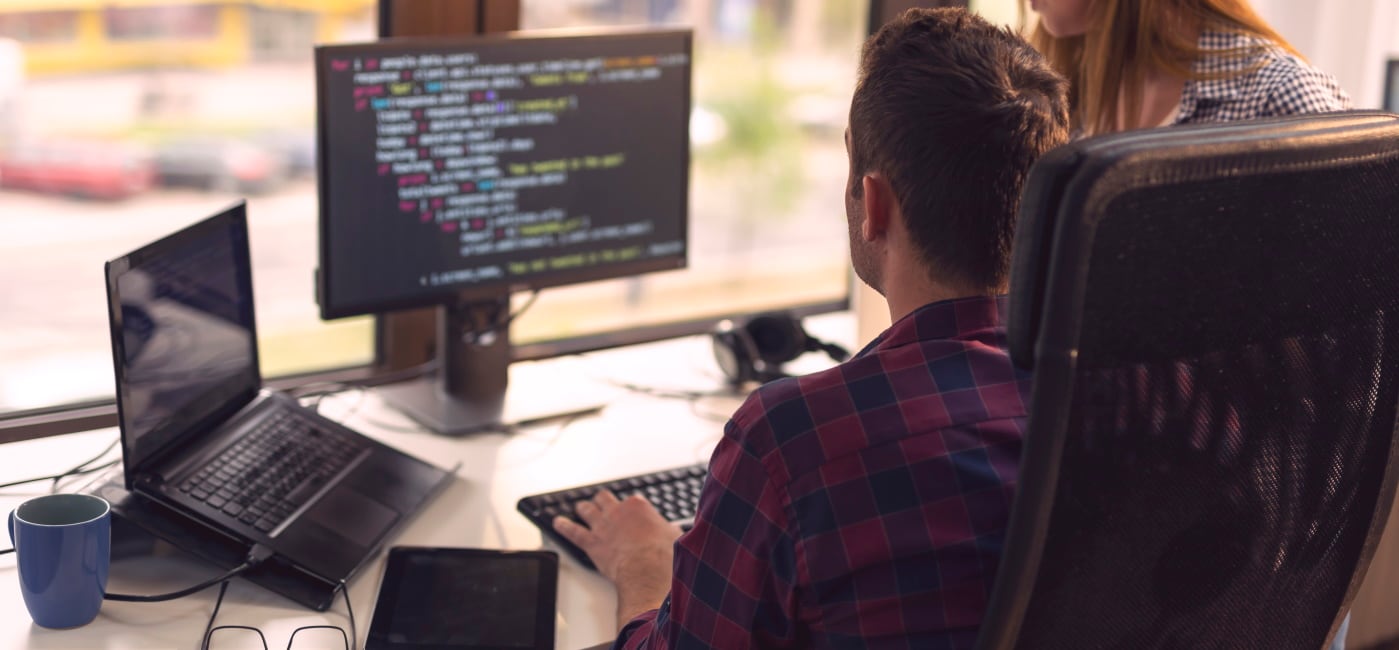 Man sitting in front of a computer monitor displaying code