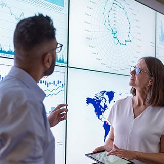 Two people look at a chart displaying data on a wall