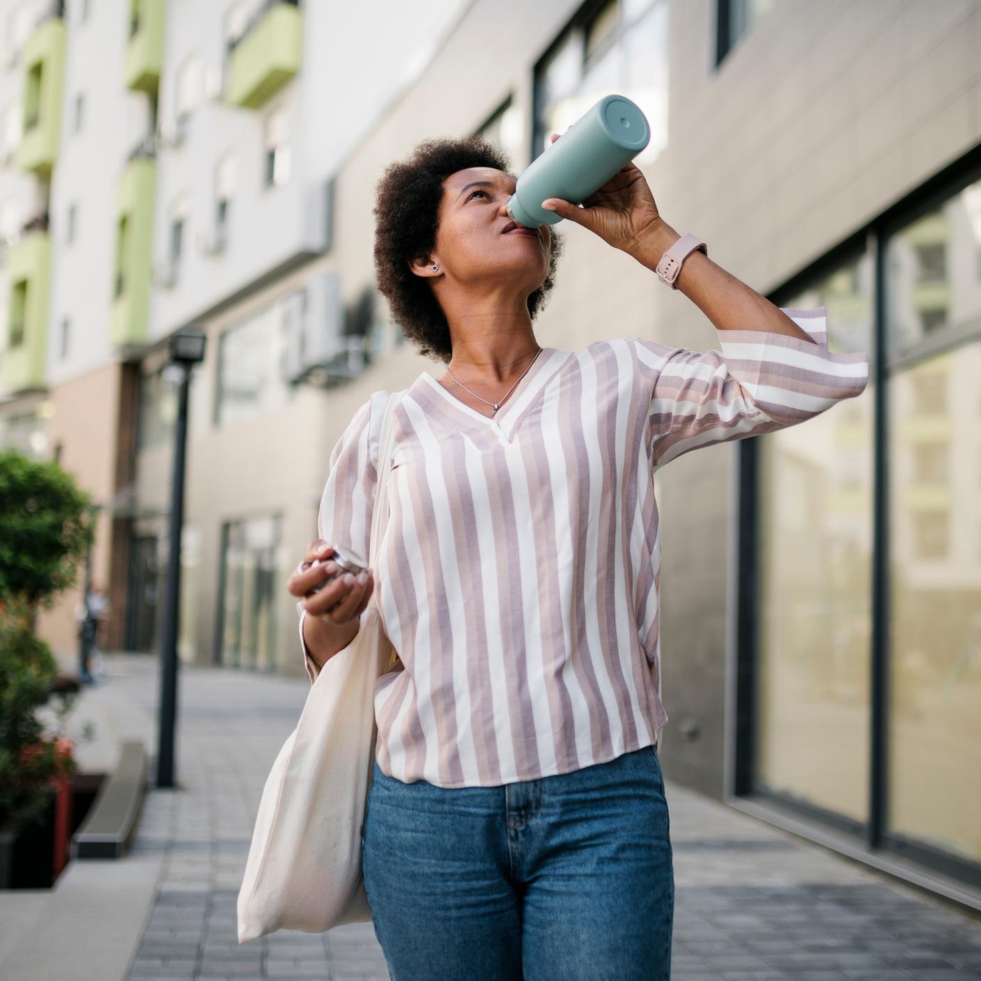 Thirsty black woman drinking water on the street