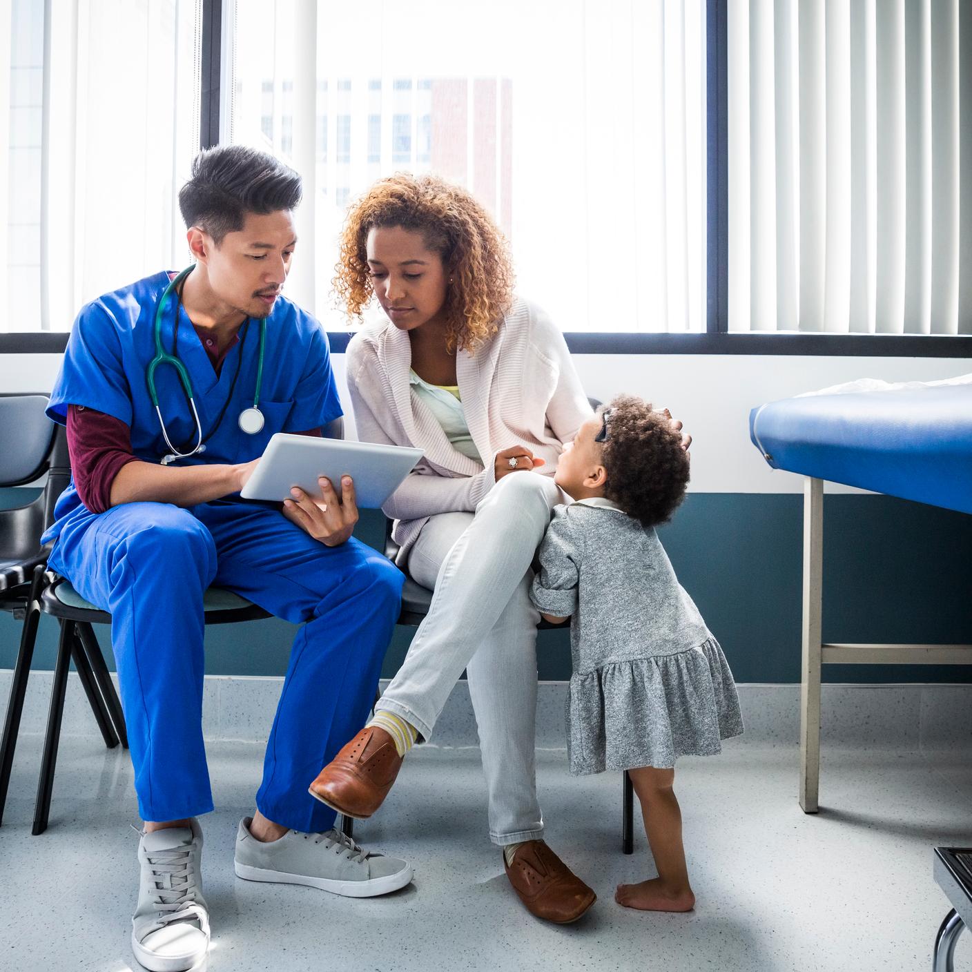 Male nurse showing digital tablet to mother by toddler in hospital