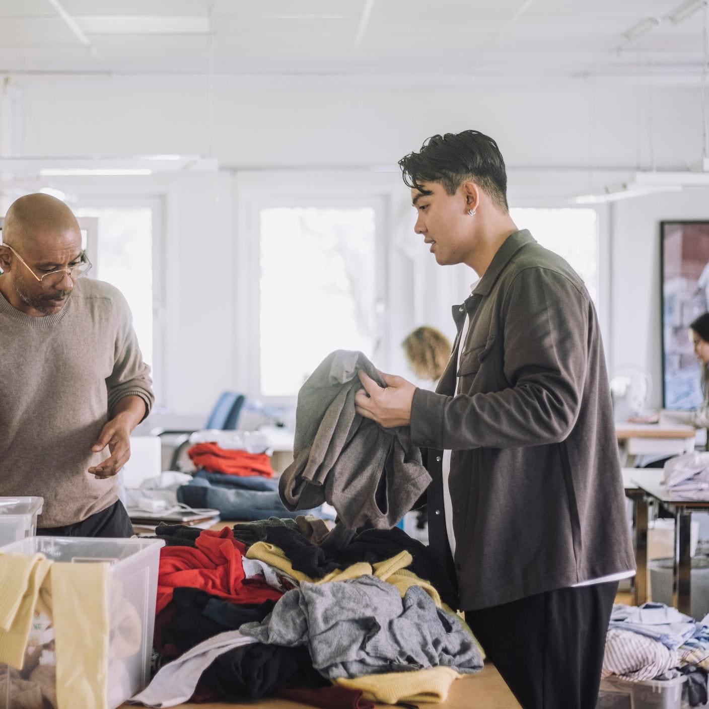 Male fashion designers discussing with each other while sorting recycled clothes at workshop