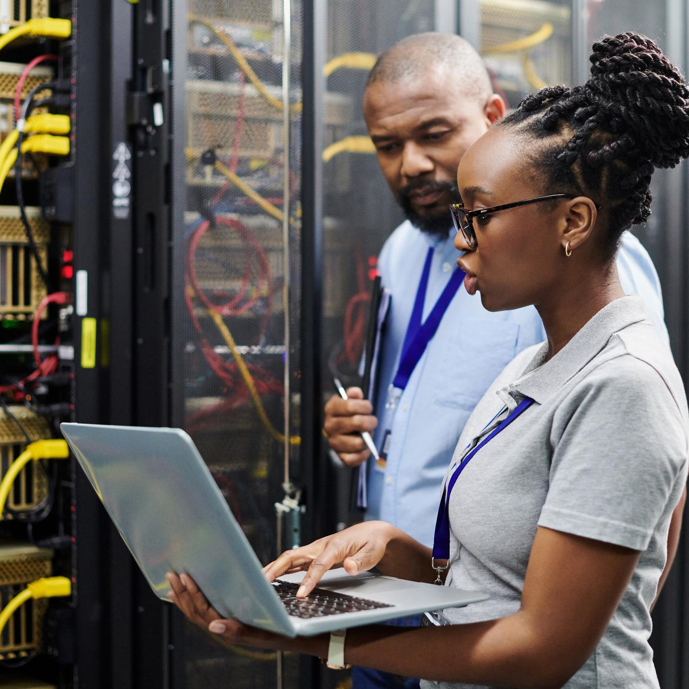 Two technicians working together on a laptop in a server room