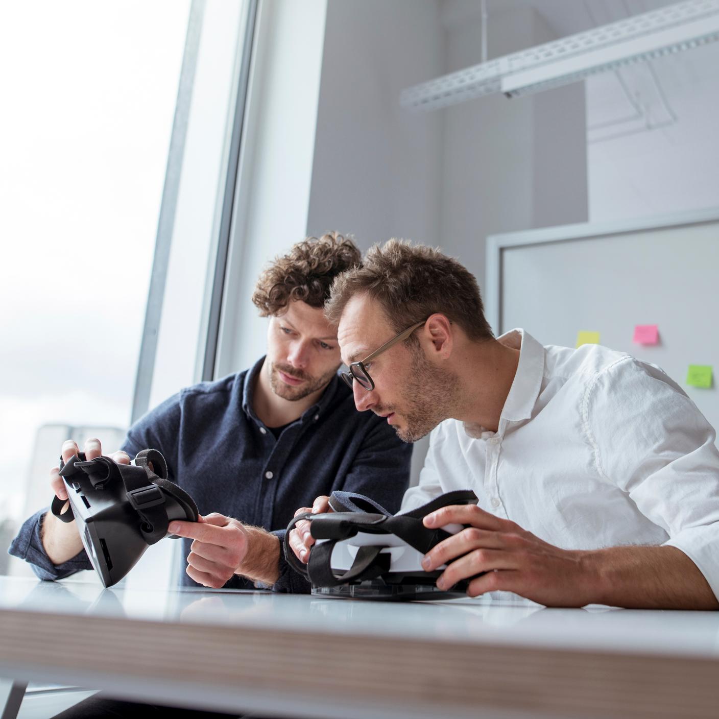 ICT - Engineers examining virtual reality simulators at table in office