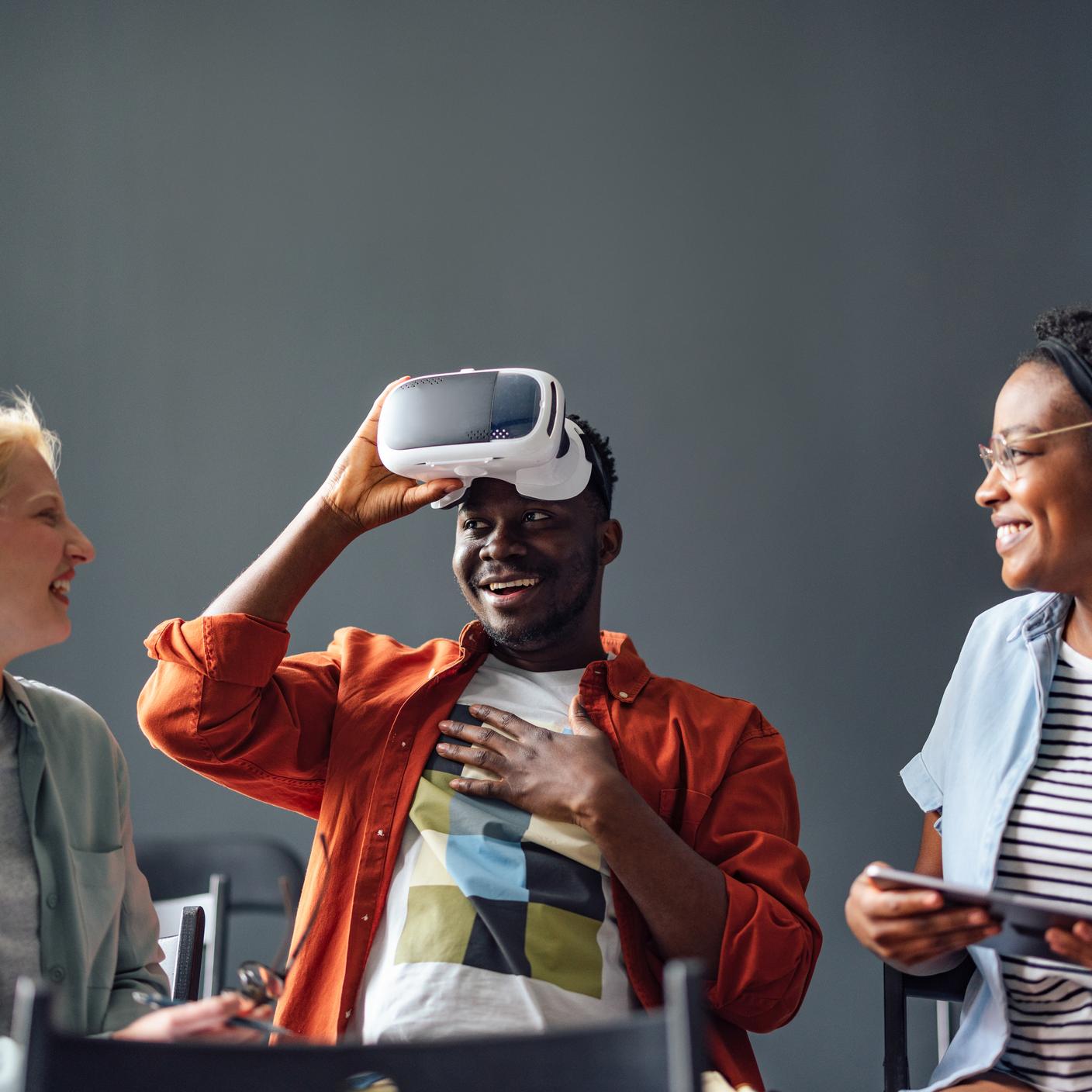 Two women smiling while their male friend is taking off virtual reality goggles