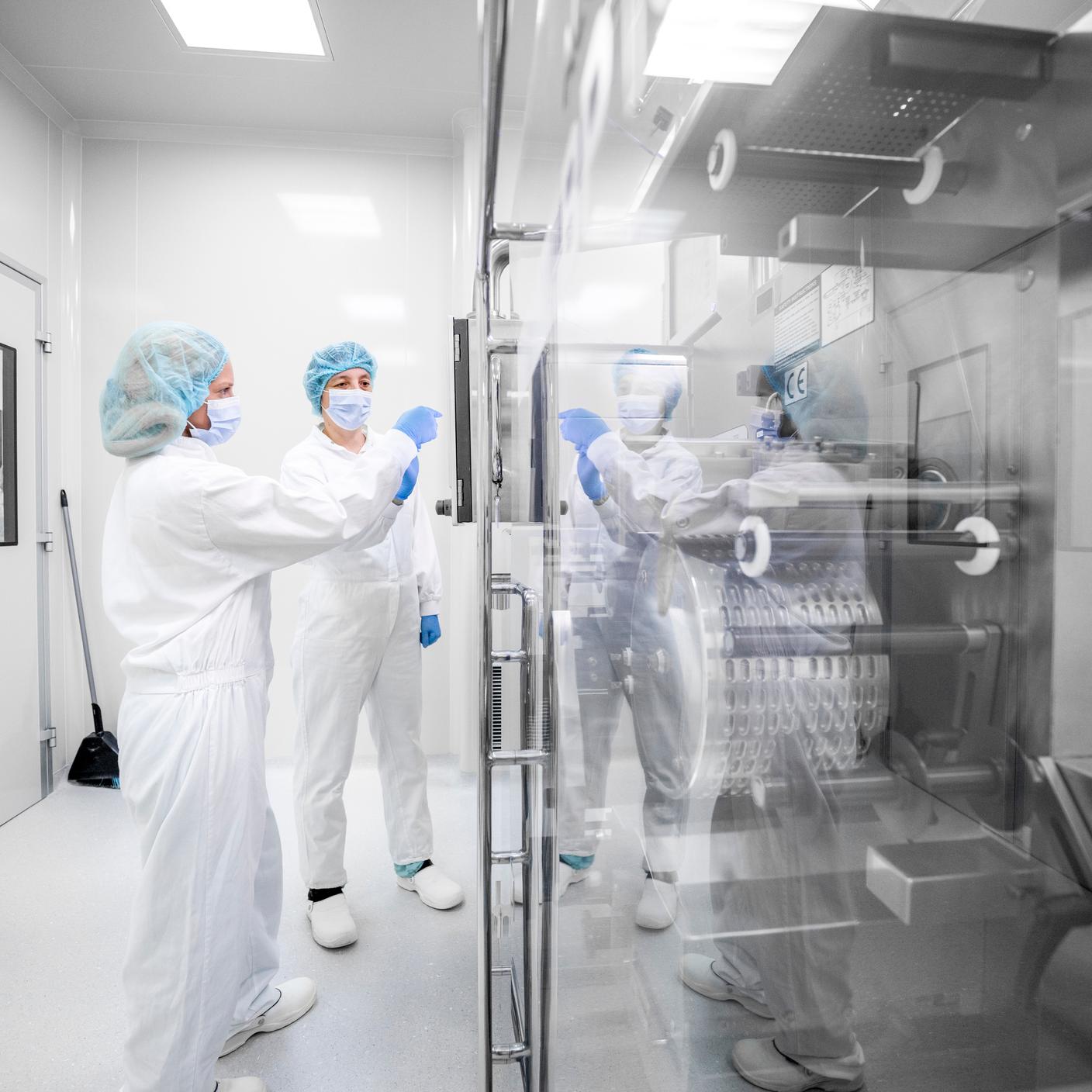 Wearing safety workwear seen in a pharmaceutical laboratory in front of the complex machine that is the part of drug manufacturing.