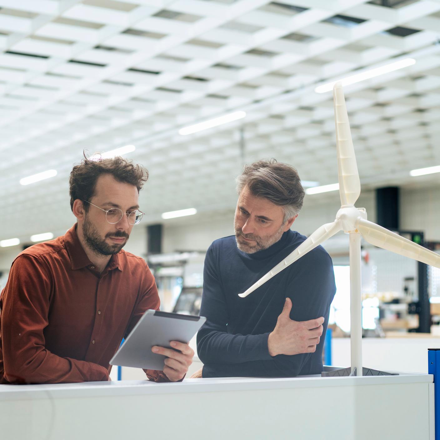 Businessman using tablet by client standing in front of wind turbine model