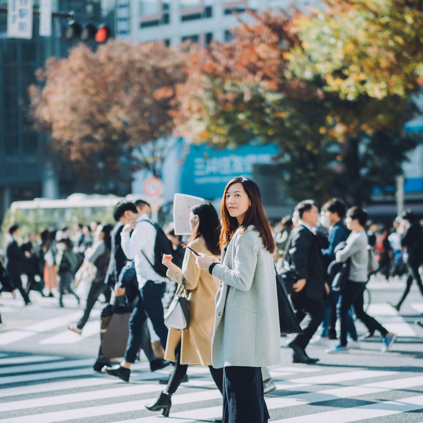 Beautiful Asian businesswoman using smartphone while walking on busy street in Tokyo