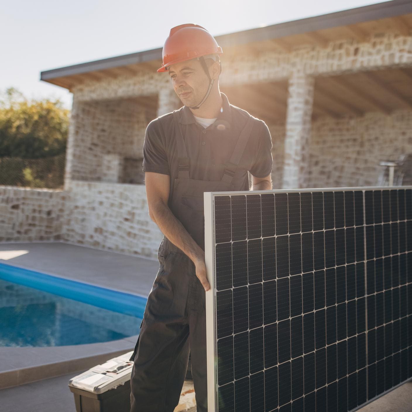 Two people, male engineers with protective helmets carrying solar panel.