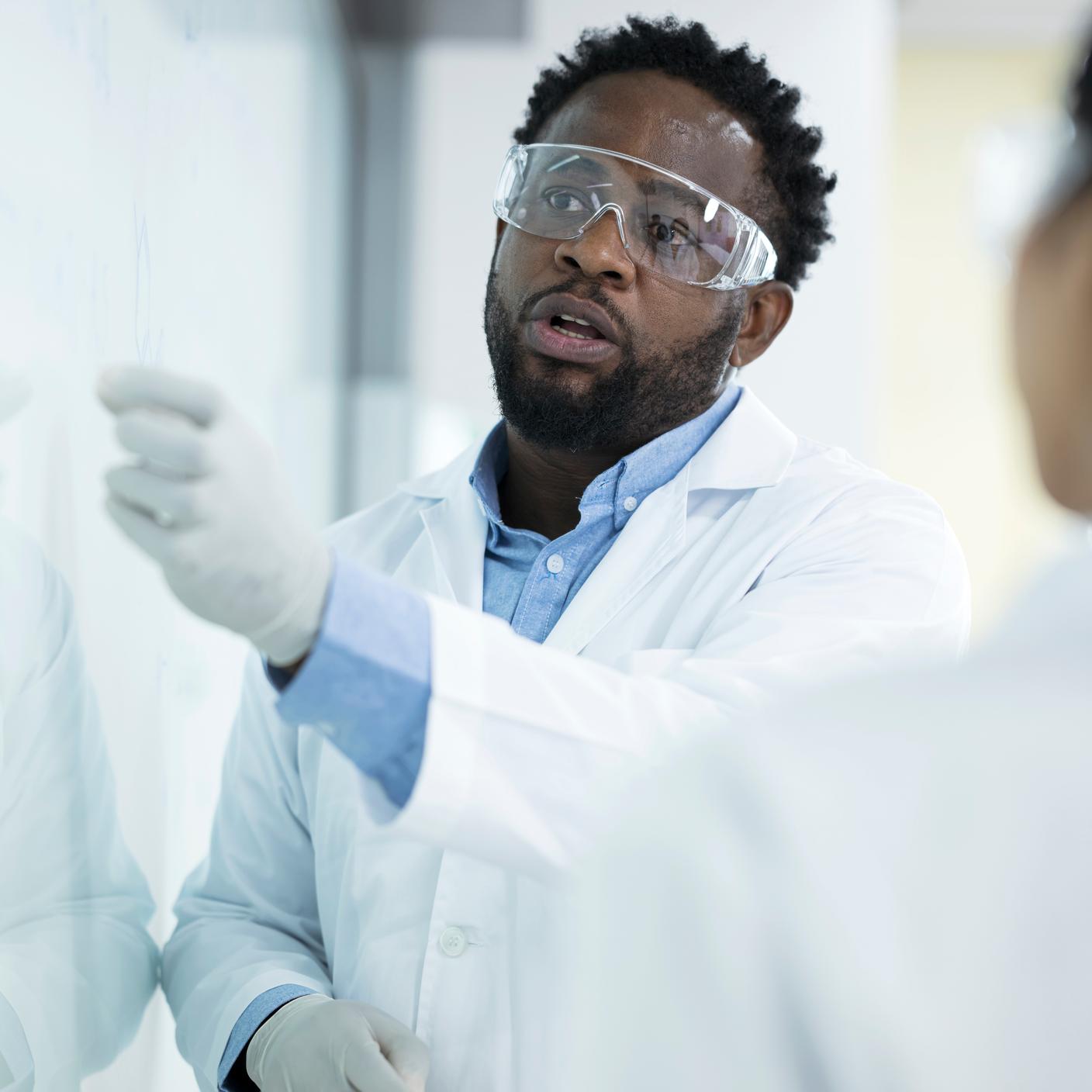 Eficiência em detrimento de rigor na decisão de testes laboratoriais. Cientista afro-americano do sexo masculino conduzindo uma discussão sobre um experimento com colegas em um quadro branco no laboratório