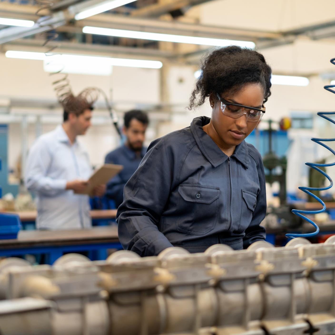 African american young woman working at an assembly production of water pumps at a factory - Incidental people at background