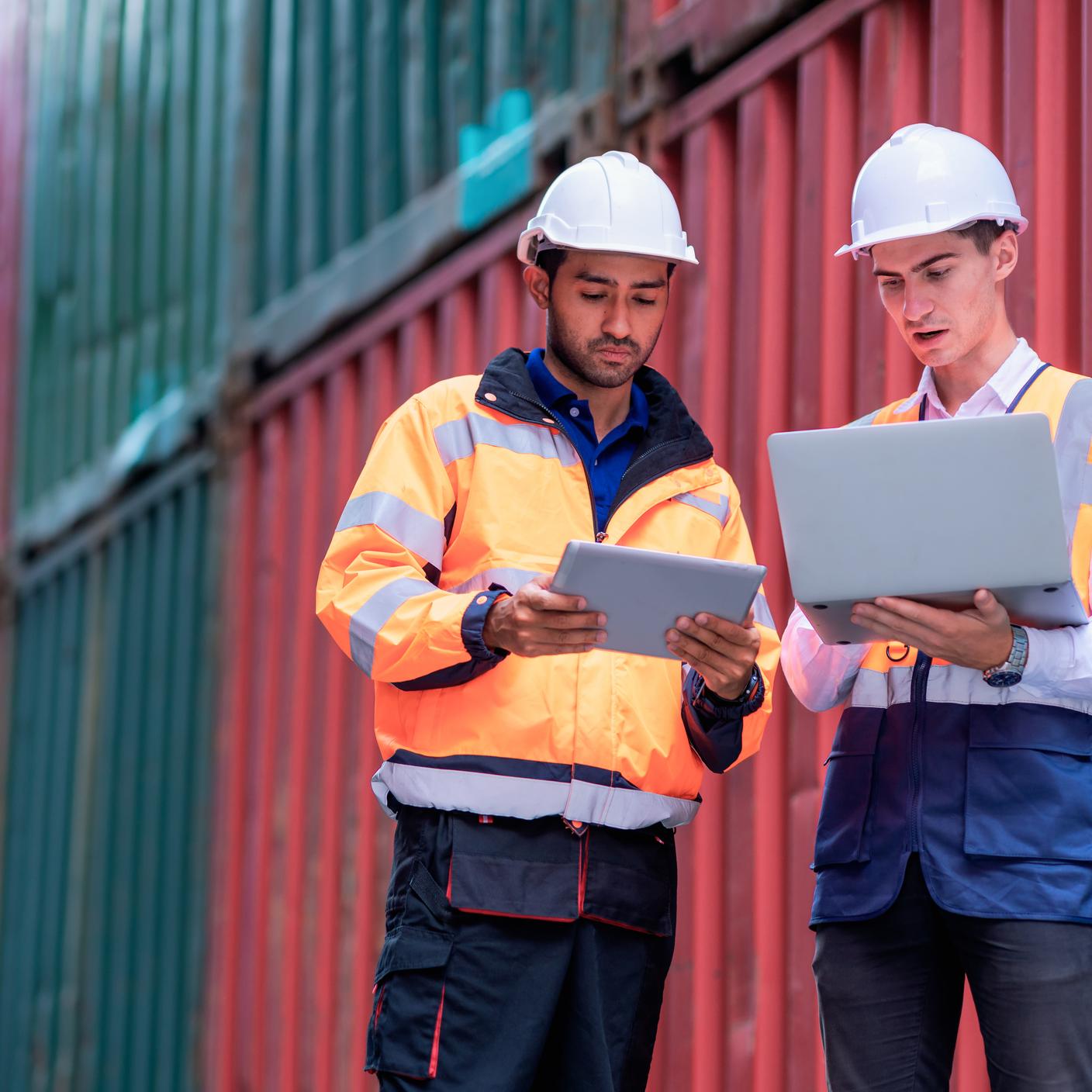 Male dock worker holding a tablet computer and explaining to his supervisor