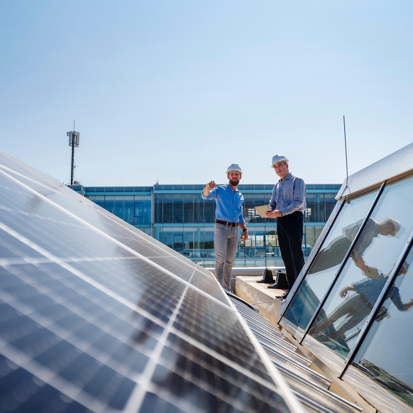 Two businessmen wearing hardhats having a meeting on the roof of a company building with solar panels