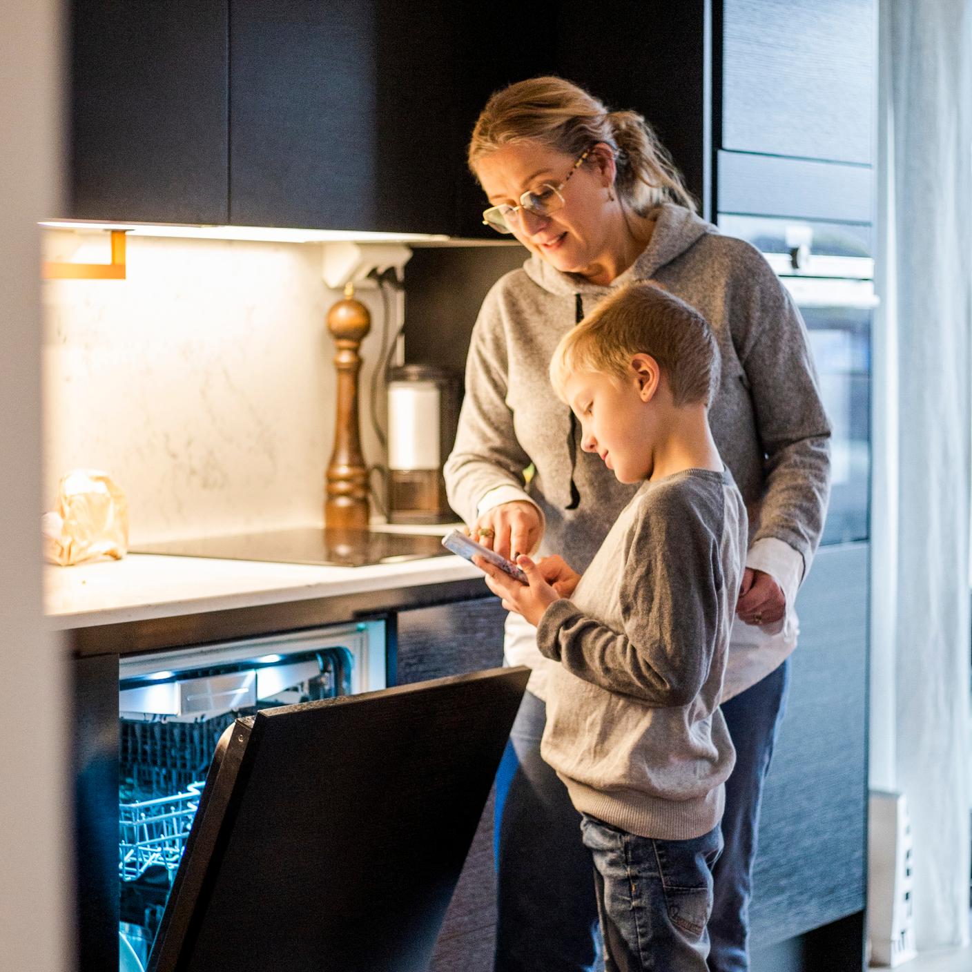 Mother teaching son to use mobile app while operating dishwasher in kitchen at home