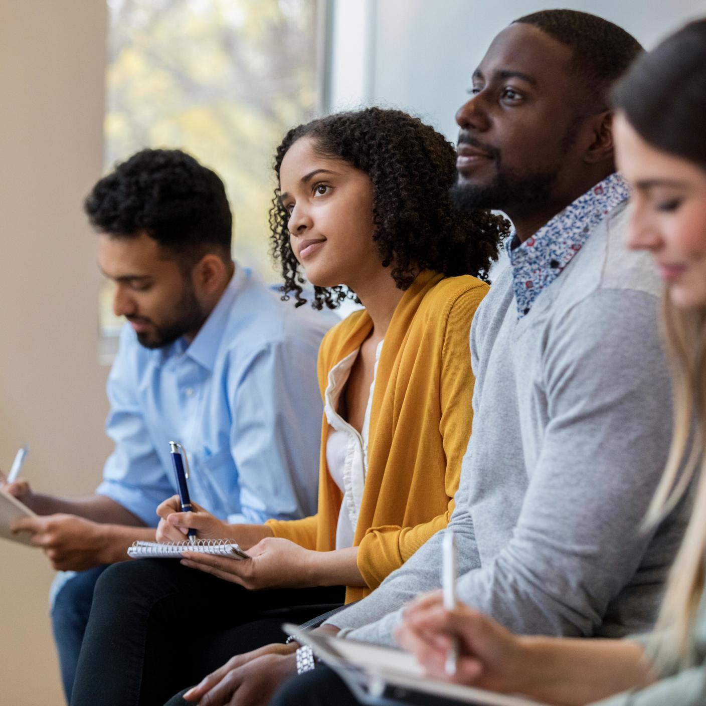 A group of business people sit in a row in a training class and taking note