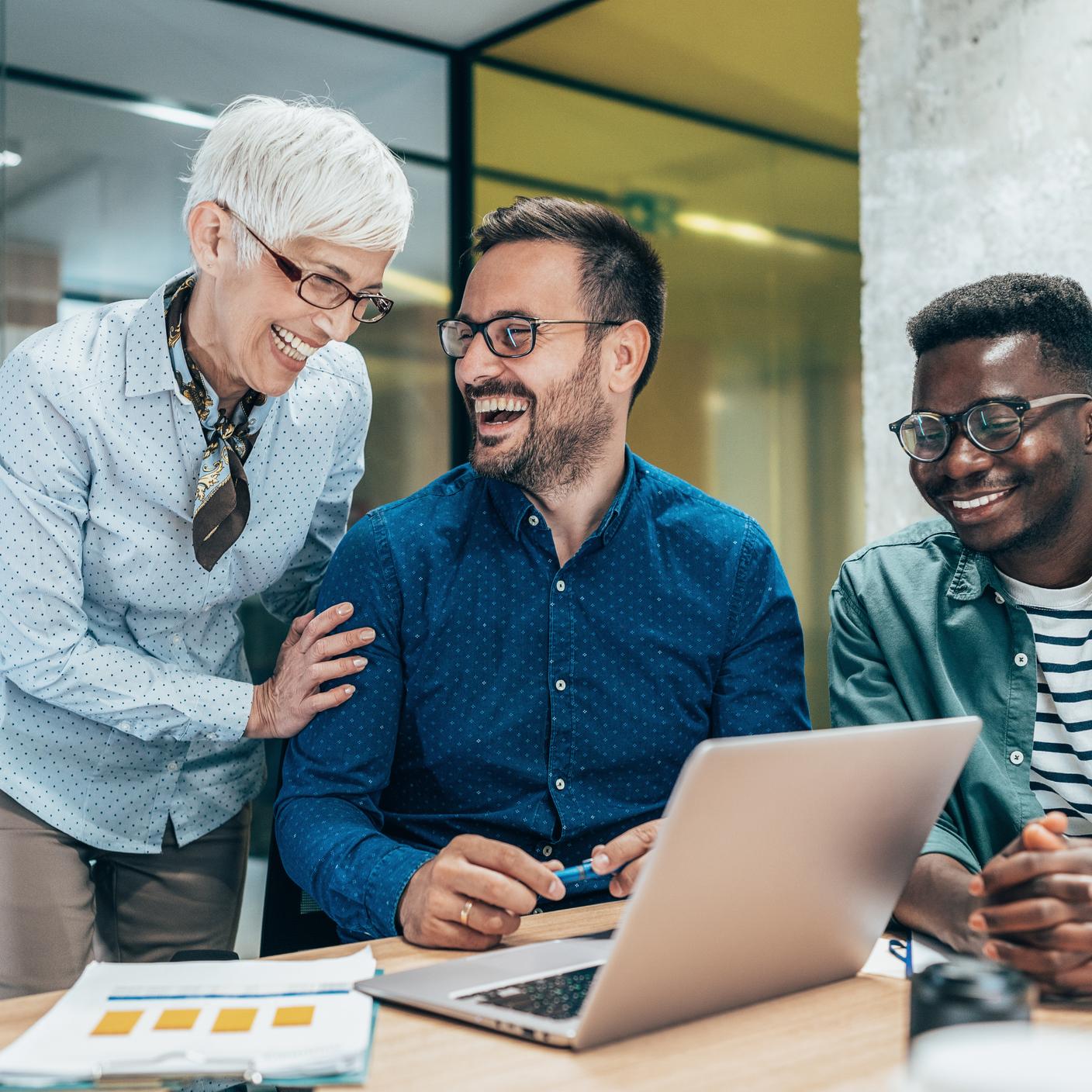 Three multi-ethnic business people discussing and laughing in modern office