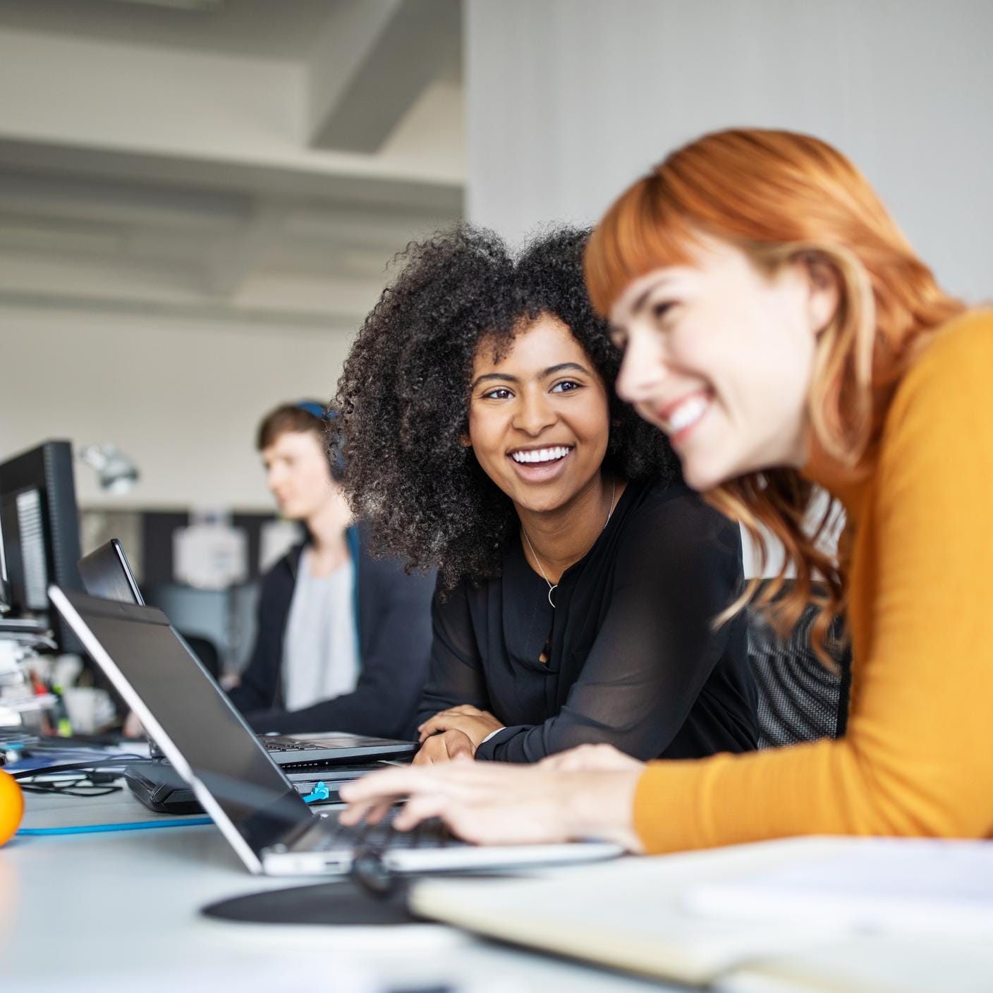 Strengthening menopause policies at Virgin Media O2 - Two young women working together on laptop with male colleague in background