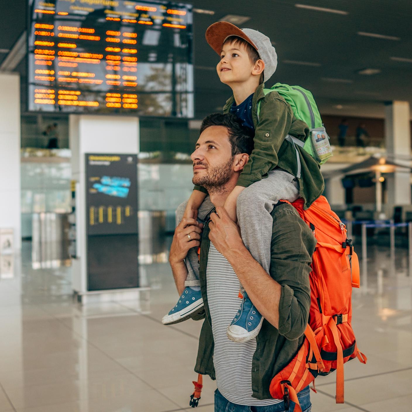 Photo of a cheerful little boy and his father, who travel together waiting for their flight at the airport.