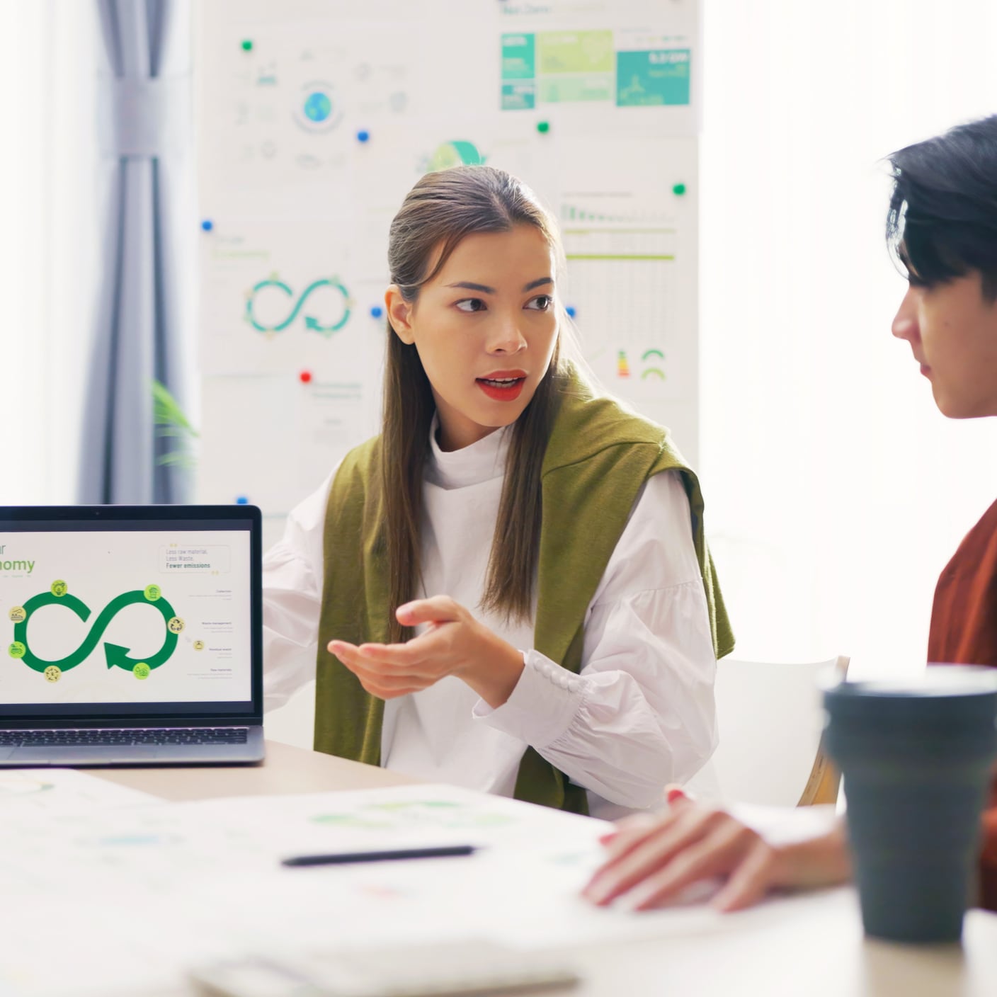 A team of professionals, including a focused woman, discusses Environmental, Social, and Governance (ESG) strategies using a laptop presentation in a bright office.