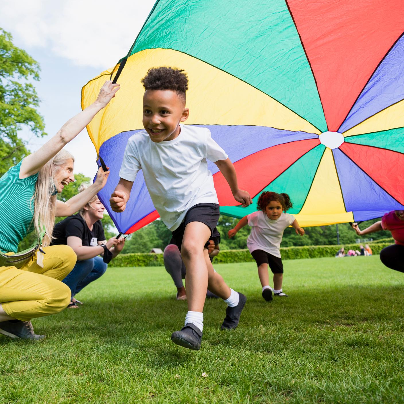 Children playing with a parachute at school during pe in the North East of England. A boy is running underneath it.