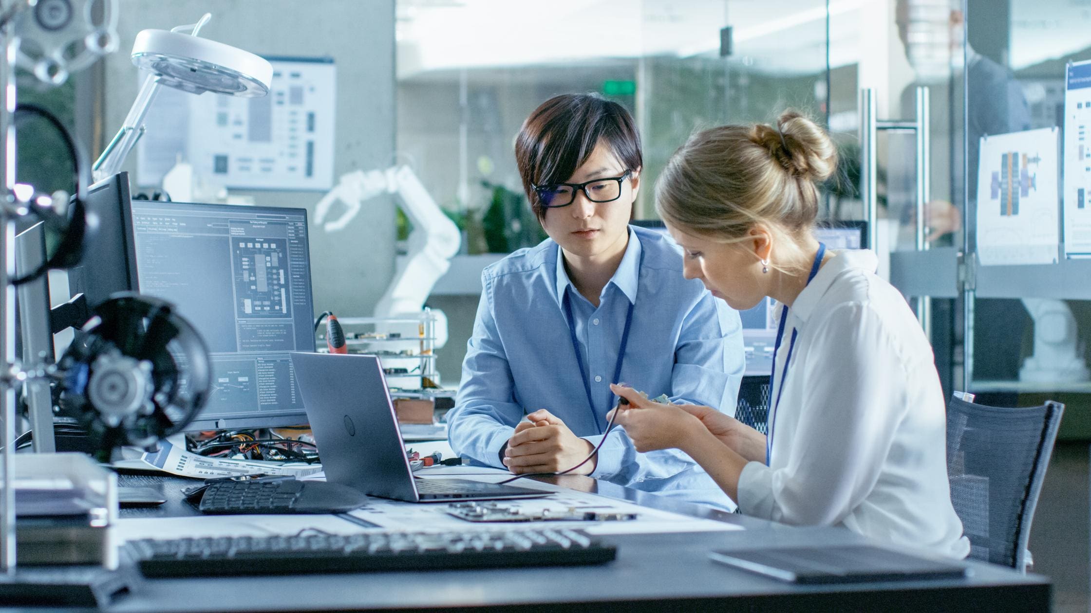 Standards - Asian Scientist Sitting at His Desk Consults Engineer about Sophisticated Coding and Programming