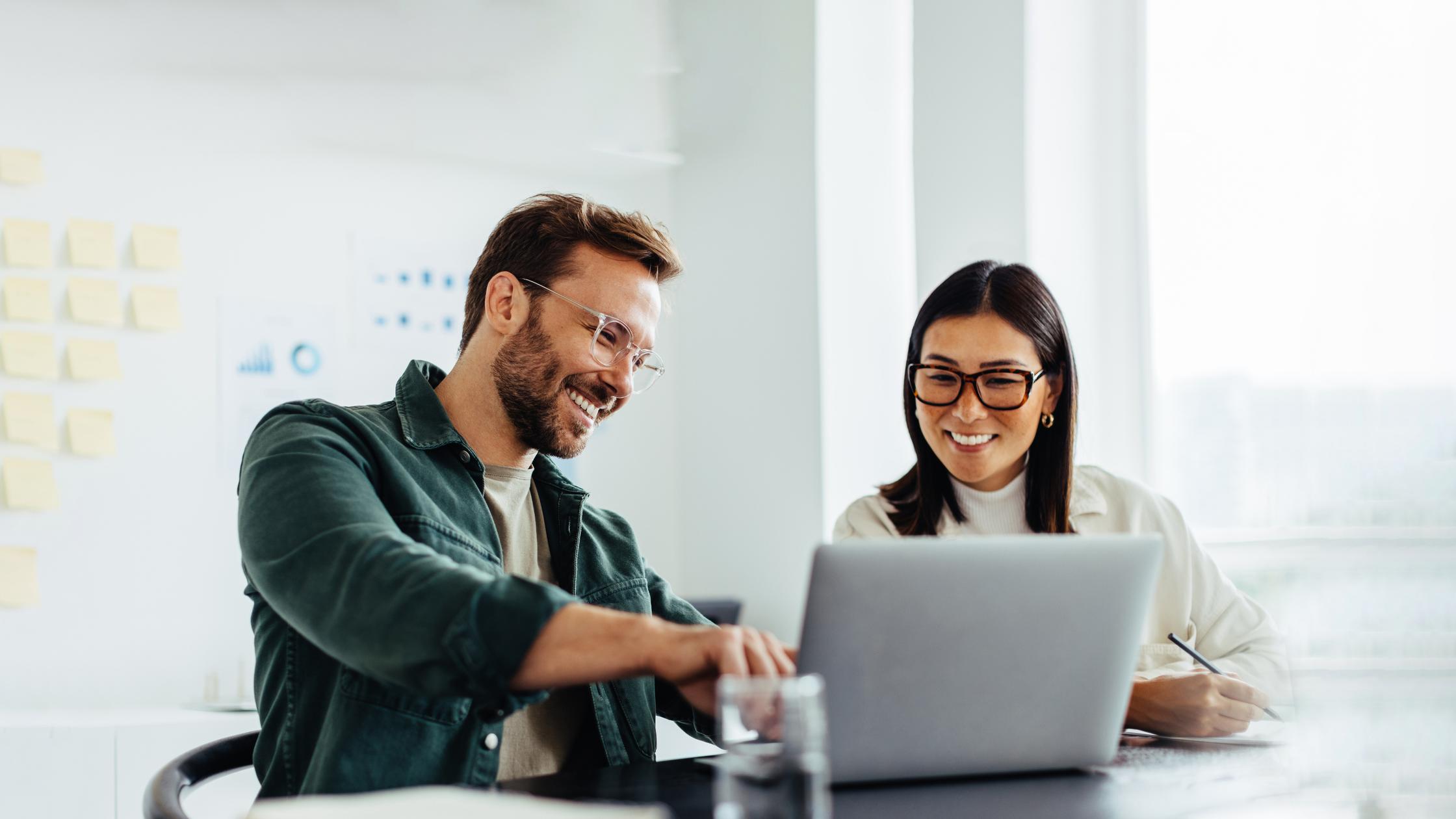 Meeting with woman and man both in glasses talking and smiling while looking at laptop